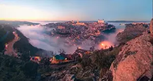 From above amazing scenery of illuminated ancient Alcazar de Toledo castle over town in misty twilight