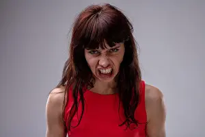 Bad News Prints: Angry temperamental woman snarling as she glowers at the camera with a fierce expression closeup over grey