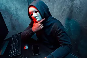 Hacker Prints: Anonymous hacker wearing face mask working on computer in dark room