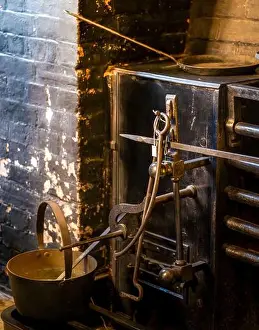 Ladle Prints: Antique cast-iron kitchen range with wrought-iron tools arrayed against a weathered brick hearth under soft ambient