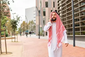 Qatar Prints: Arab businessman in traditional clothes making call on cellphone