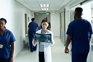 Female Doctor Prints: Asian female doctor studying x-ray photo standing in busy hospital corridor