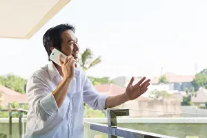 Affluent Prints: Asian man telephoning on balcony with mobile phone