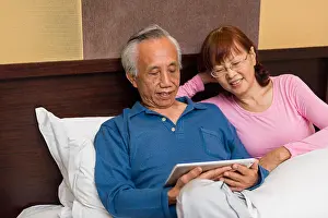 Spectacles Prints: Asian senior couple sharing and enjoying mobile entertainment. Copy space on left
