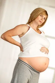 Curtains Prints: ATTRACTIVE HEALTHY YOUNG PREGNANT WOMAN STANDING IN FRONT OF WINDOW WITH HANDS ON LOWER BACK WITH EXPRESSION OF PAIN