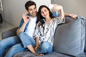 Lifestyle Home Prints: Attractive young couple relaxing on a couch at home, hugging, taking a selfie