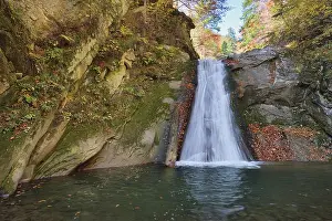 Autumn waterfall and creek woods with yellow trees foliage and rocks in forest mountain