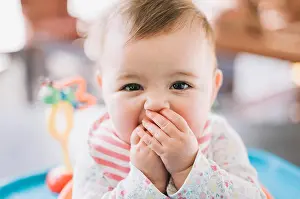 Baby Girl Prints: A baby girl with her hands covering her mouth, looking at the camera