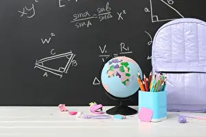Holder Prints: Backpack, stationery and globe on white table against green chalkboard with formulas