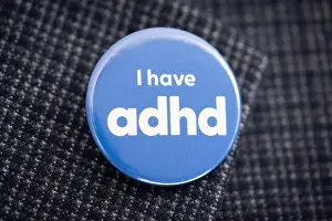Attached Prints: A badge featuring the words I have ADHD is seen being worn on the lapel of a blue blazer