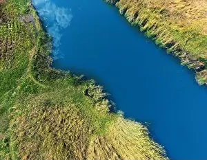 Banks of the river are covered with greenery with a tourist lying on the bank. Shooting from a height