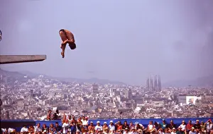 Barcelona Spain, August 1992: Male diver competes in the 10-meter platform diving finals at the Summer Olympics, with downtown Barcelona and the spire