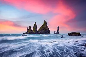 Basalt rock formations Troll toes on black beach with pink sunset clouds. Great purple sky glowing on background. Reynisdrangar, Vik, Iceland