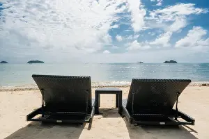 Beach chairs on the sandy beaches for tourists to sit and relax with soft ocean waves breaking on beach. Summer travel vacation and holiday concept