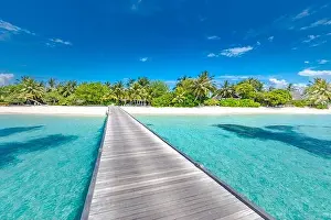 Beach with jetty on a tropical island. Maldives luxury paradise landscape. White sand over blue lagoon into palm tree covered island. Exotic travel