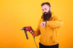 Belt Prints: Bearded man wearing yellow hoodie hoding power drill and looking at his watch over yellow background