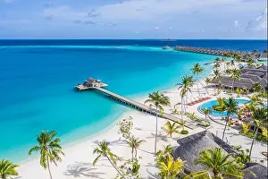 Beautiful aerial view of poolside and resort beach with wooden pier jetty. Luxurious tropical hotel landscape swimming pool deck chairs loungers palms