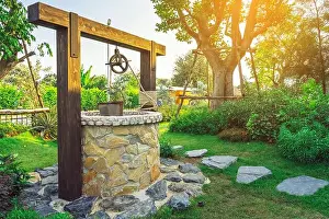 Pail Prints: Beautiful artesian well made by stones and wheel pulley with metal bucket and rope in peaceful garden atmosphere