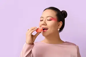 Beautiful Asian woman eating tasty Japanese mochi on color background