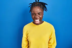 Beautiful black woman standing over blue background angry and mad screaming frustrated and furious