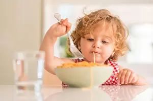 Messy Prints: Beautiful blond child eating spaghetti with fork at home