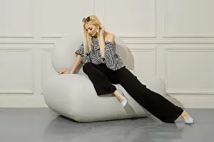 Crossed Prints: A beautiful blond-haired woman in fashionable boho style clothes sits with her legs crossed in a soft bean bag chair