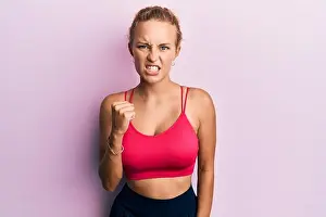 Fist Prints: Beautiful caucasian woman wearing sportswear angry and mad raising fist frustrated