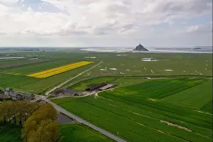 Beautiful drone view of famous Le Mont Saint-Michel tidal island with blue sky and yellow fields of rapeseed
