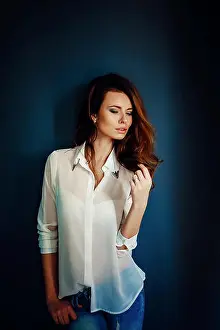 Grief Prints: Beautiful girl standing near the dark blue wall in darkness in blue jeans and white shirt