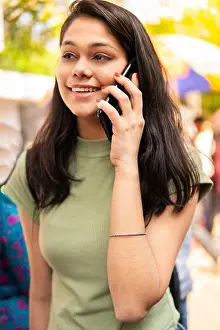 Toothy Smile Prints: Beautiful happy late teen girl walking on market street and talking on smartphone at day time