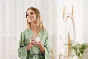 Healthy Home Prints: Beautiful happy woman with cup of hot drink wearing robe in bathroom. Space for text