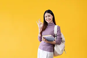 Yellow Background Prints: A beautiful and happy young Asian female college student with a backpack holding her school books
