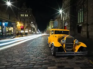 Taxi Prints: Beautiful old yellow car on cobbled street at night in medieval Edinburgh