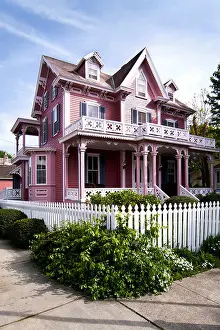 Porch Prints: Beautiful pink Victorian house with porch and balcony surrounded by a white picked fence