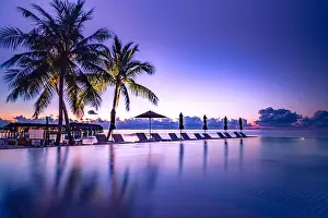 Beautiful poolside and sunset sky. Luxurious tropical beach landscape, deck chairs and loungers and water reflection. Infinity pool, sunset beach view