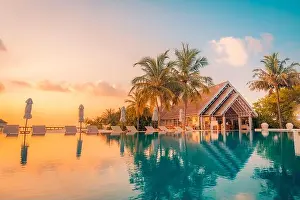 Beautiful poolside and sunset sky. Luxurious tropical beach landscape, deck chairs and loungers and water reflection. Amazing vacation, summer holiday