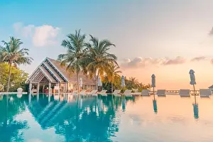 Beautiful poolside and sunset sky. Luxurious tropical beach landscape, deck chairs and loungers and water reflection. Amazing vacation, summer holiday