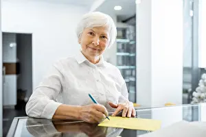 Patients Prints: Beautiful senior woman signing some medical documents stannding at the hospital reception