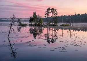 Beautiful sunrise landscape with misty mood and calm lake at foggy summer morning in Finland