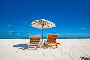 Beautiful tropical beach, two sun beds, loungers, umbrella under palm tree. White sand, sea view horizon, blue sky, calmness and relax resort scenery