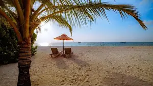 Beautiful tropical sunset scenery, two sun beds, loungers, umbrella under palm tree. White sand, sea view with horizon, colorful twilight sky, vibes