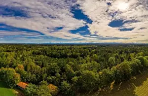 A beautiful view over a green forest at the early autumn with an idyllic house in the foreground, shot by a drone
