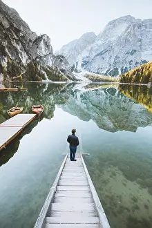 Alto Adige Prints: Beautiful view of a young man standing on wooden stairs watching the sunrise at famous Lago di Braies the Dolomites
