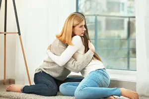 Helpless Prints: Beautiful woman hugging depressed friend while sitting on floor at home
