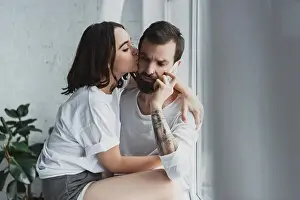 beautiful woman kissing man talking on smartphone at home