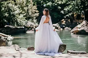 Blue Day Prints: a beautiful woman in a long white dress looks into the distance at a beautiful lake with swans rear view