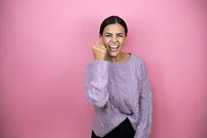Braids Prints: Beautiful woman wearing a casual violet sweater over pink background angry and mad raising fist frustrated