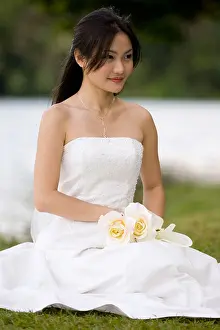 Asians Prints: A beautiful young asian woman in a wedding dress sitting by the edge of a lake