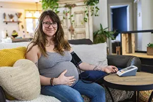 Digitally Prints: A beautiful young pregnant woman carries out prenatal health checks at home using a digital sphygmomanometer to measure