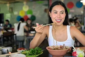 Noodle Prints: Beautiful young Thai woman eating famous Thailand street food boat noodles served at local restaurant